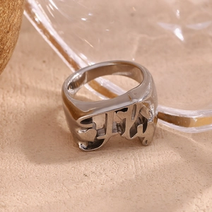 Macro shot of silver cutout letter ring with polished stainless steel finish on beige base
