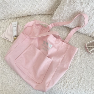 Détail du sac cabas rose en toile avec broderie nœud sur la poche texturée