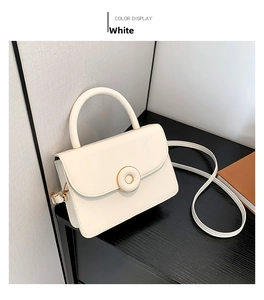 Detail view of white minimalist handbag with gold round magnetic buckle and top handle