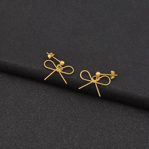 Detailed close-up of golden bow-shaped stud earrings with a central bead on a dark textured surface
