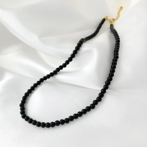 Elegant black agate beaded necklace with gold clasp laid on white silk fabric detail