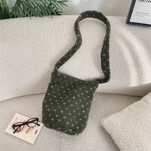 Detail of dark green faux shearling shoulder bag with white floral pattern on a sofa