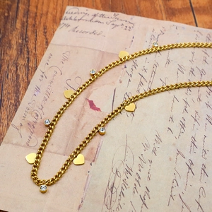 Close-up of gold heart charms and sparkling round crystals on a delicate chain necklace