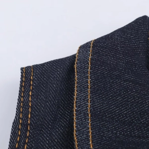 Detailed close-up of dark indigo denim fabric with reinforced orange double-row stitching