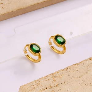Detailed macro view of gold oval earrings with green gemstones on minimalist stone blocks