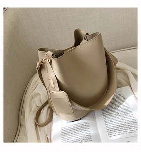 Gros plan d'un sac seau beige avec texture litchi et deux bandoulières sur un canapé