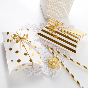White pillow favor boxes with gold foil dots and stripes, tied with gold ribbons