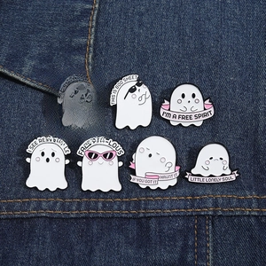 Close-up of cute pink ghost enamel pins with funny captions on denim fabric background
