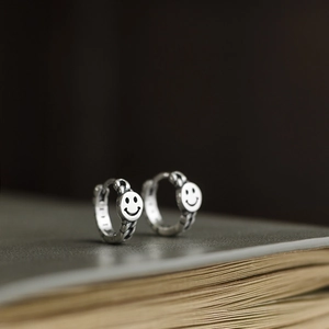 Macro detail of vintage silver smiley face hoop earrings on antique book pages