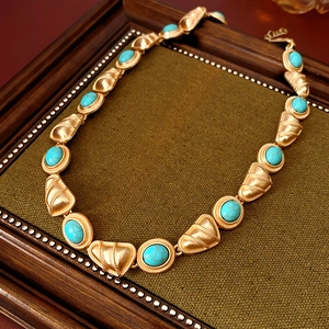 Gros plan d'un collier vintage doré avec pierres turquoise ovales sur tissu vert