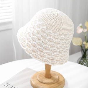 Detailed knit texture of a cream hollow-out bucket hat on a wooden display stand