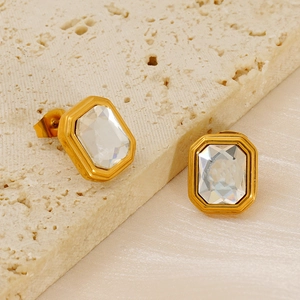 Detail view of rectangular white zircon earrings with gold plating on stone and silk background
