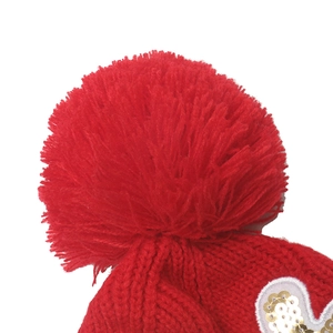 Close-up of red knit hat with large plush pompom and sequin reindeer embroidery