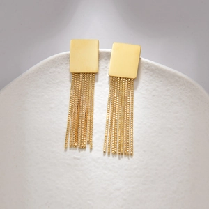 Macro shot of gold fringe leaf earrings with tassel chains on a white ceramic plate