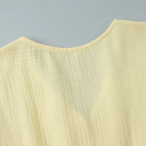 Detail of a yellow cotton dress showing round neckline and vertical pleated texture