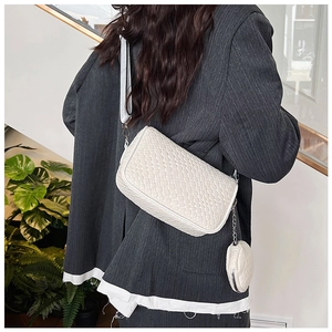 Detail of white woven crossbody bag with small round coin purse charm on a shoulder strap