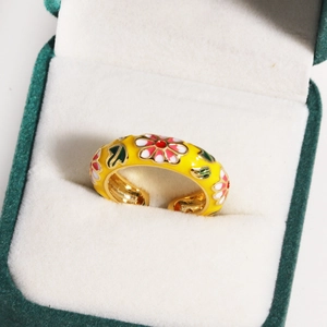Macro shot of yellow enamel flower ring with red blossoms on green velvet jewelry box