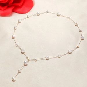 Macro view of gold chain necklace with white freshwater pearls on white silk background