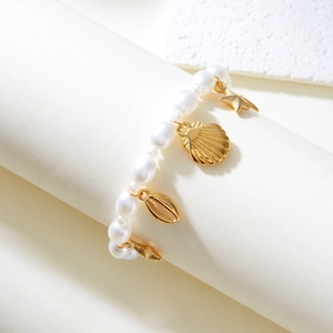 Detail of pearl bracelet featuring golden starfish, shell, and conch charms on white background