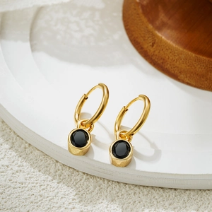 Macro detail of 18K gold-plated oval black stone pendant on minimalist hoop earring