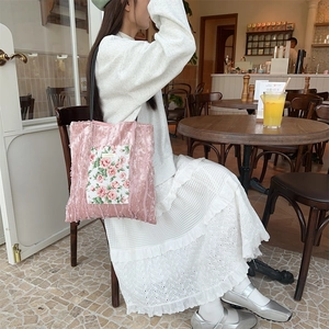 Pink velvet tote bag with rose floral patch and black shoulder straps in a cafe setting