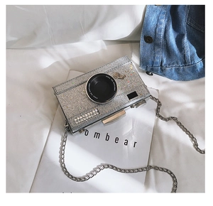 Detailed view of silver sequin camera-shaped handbag with rhinestone lens and chain strap