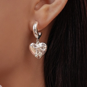 Macro view of silver heart earrings featuring sparkling zirconia bows on the earlobe