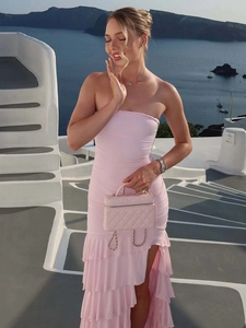 Pink strapless tiered maxi dress with waist cinching and side slit on white architecture