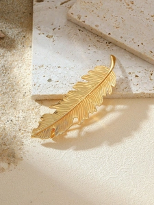 Macro detail of a golden leaf hair clip with intricate textures on a natural stone base