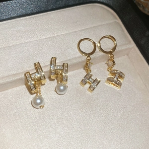 Detailed macro view of 14K gold plated H-letter pearl earrings with cubic zirconia stones