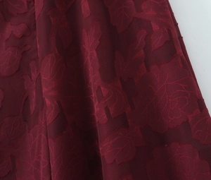 Makroaufnahme von dunkelrotem Jacquard-Stoff mit floraler Prägestruktur auf einem Kleid