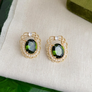 Detailed macro shot of vintage gold lace earrings with emerald stone and pearl border