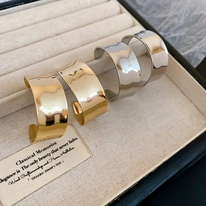Nahaufnahme breiter Metall-Ohrklemmen mit unregelmäßiger Wellentextur in Gold- und Silberoptik