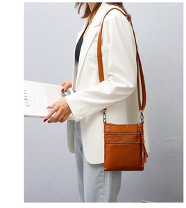 Detail of caramel brown PU leather crossbody phone bag with three zipper pockets and tassel