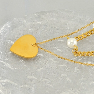 Detailed close-up of double-layer gold heart pendant with single pearl on a stylish chain