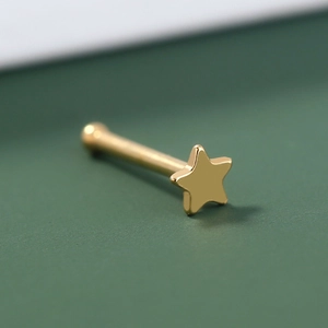 Detailed close-up of golden star-shaped stainless steel nose stud on dark background