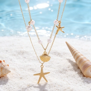 Dettaglio collana doppia dorata con stella marina, conchiglia e perle sulla spiaggia