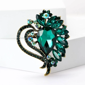 Detailed view of a vintage heart brooch with emerald gemstone and crystals on gold base