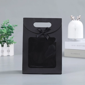Detail of black paper gift bag with transparent square window and ribbon bow handle