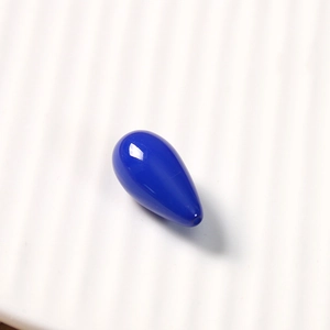 Macro view of a glossy blue resin teardrop pendant on a white textured background