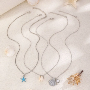 Dettaglio della collana boho a tre strati con stella marina, conchiglia e perla sulla sabbia