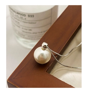 Detail of a white round pearl pendant on a silver S925 chain over a wooden frame