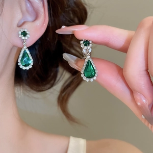 Macro shot of green teardrop earrings with a petal-shaped diamond halo in gold finish