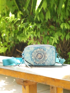 Blue gradient crossbody bag with mandala patterns on a wooden bench outdoors