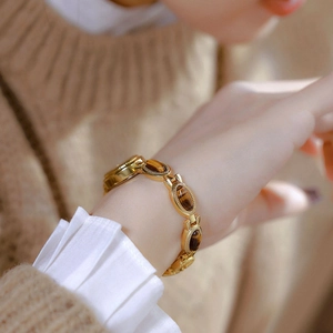 Close-up of a gold luxury watch with tiger eye stone band on a female wrist