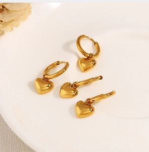 Macro shot of minimalist gold heart hoop earrings on white ceramic plate with dried flower