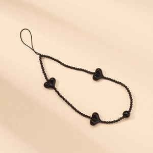 Detail of handmade black beaded phone strap with acrylic heart charms on beige background