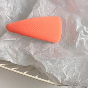 Detailed macro view of a coral-colored triangular sponge puff on white tissue paper