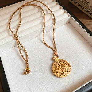 Dettaglio macro del ciondolo dorato traforato con motivi orientali in scatola regalo