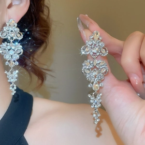 Detail showing long silver drop earrings with zircons being worn and held by hand